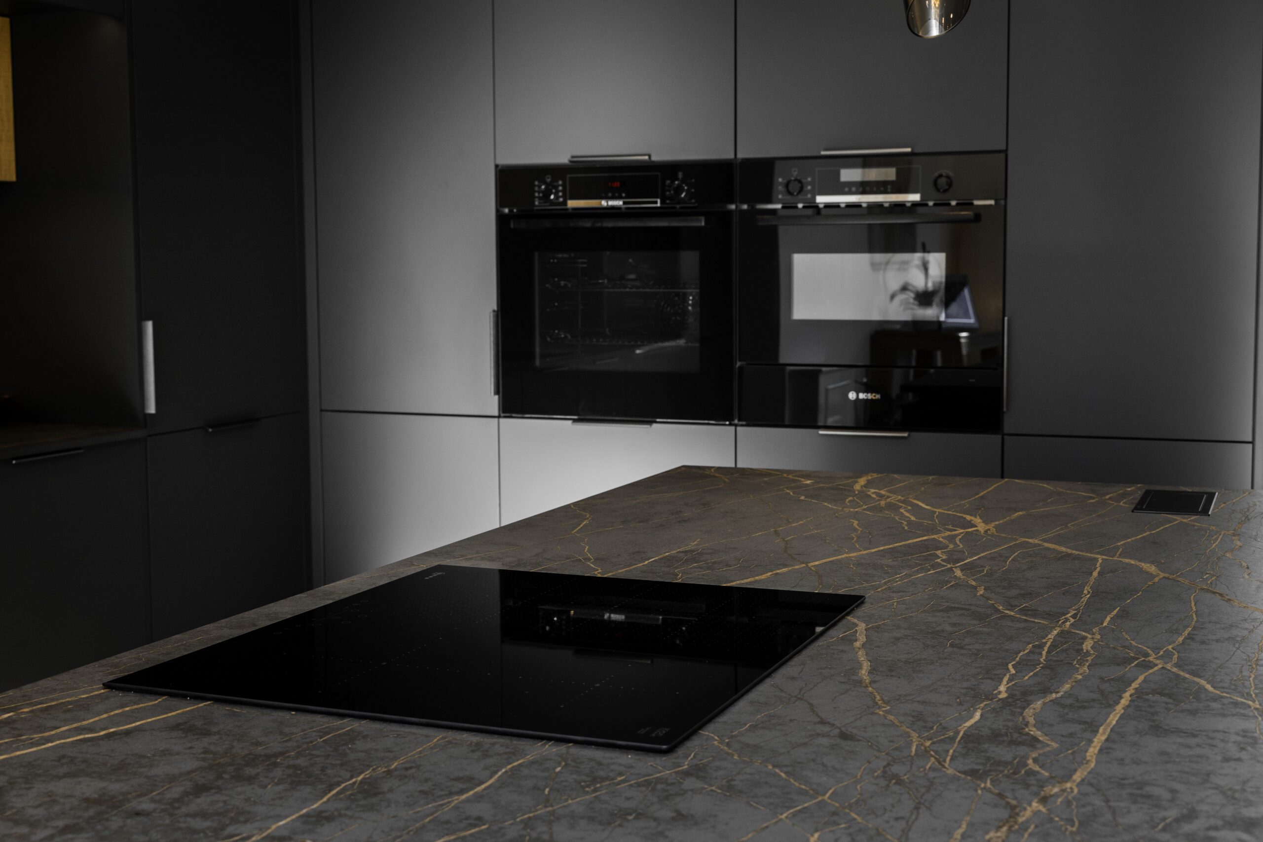Close-up of a flush black induction hob set into a Laurent Porcelain worktop with gold veining.