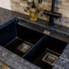 Close up of an undermount double bowl sink set into Steel Grey leather Granite worktop, showing the textured finish and clean cut-out lines.
