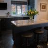 Angled view of an Ivory Spice Granite island worktop with breakfast bar stools, showing the polished Granite finish and clean edge detail in a dark kitchen.