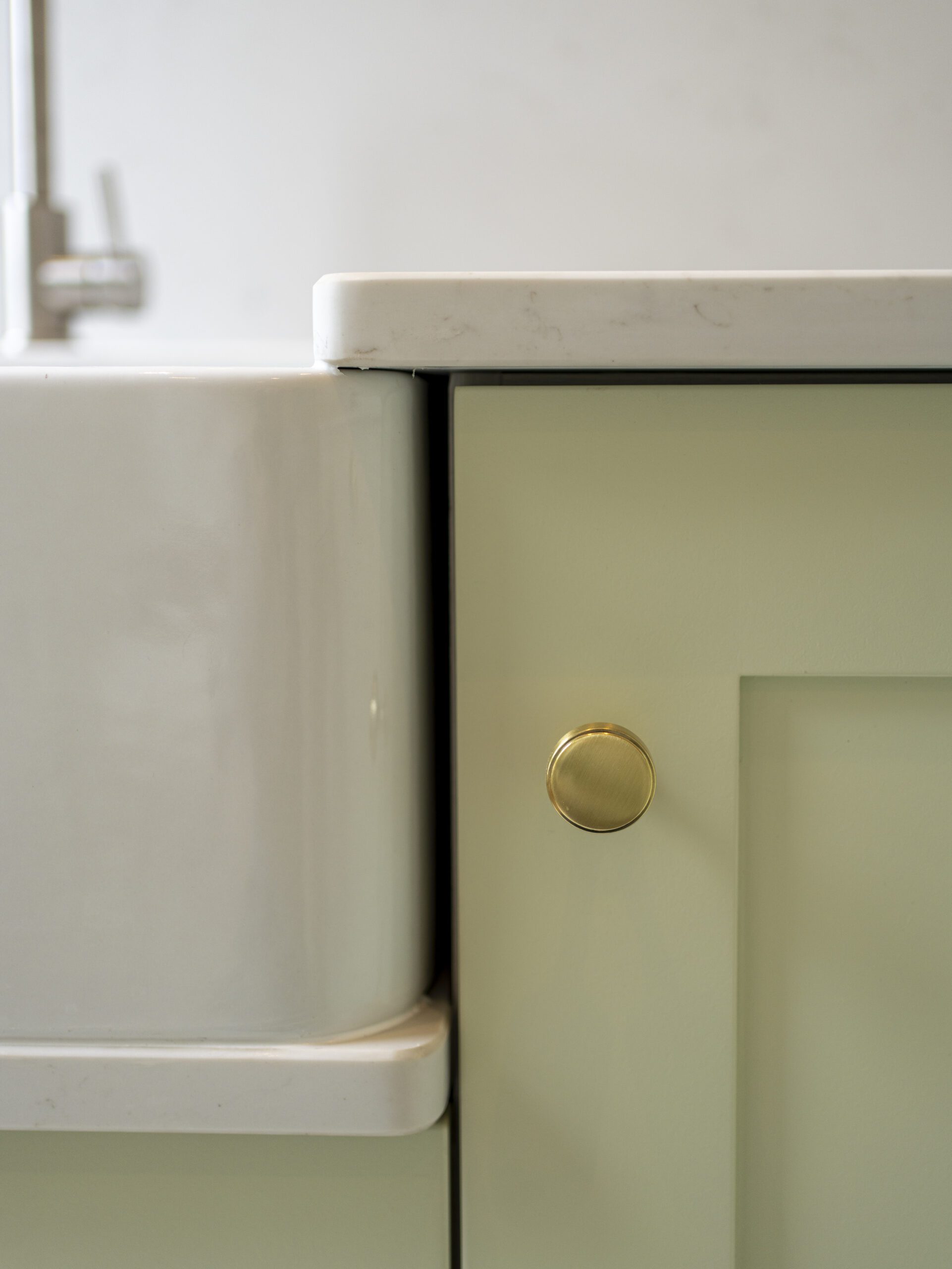 Close up of Carrara Quartz worktop around white inset sink with brass knob cabinetry