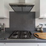 Grey speckled Quartz worktop with matching splashback behind a gas hob and cooker hood