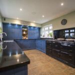 Wide angle view of a blue kitchen with Absolute Black Granite worktops, showing the sink run in the foreground and the main cooking area with a range cooker.