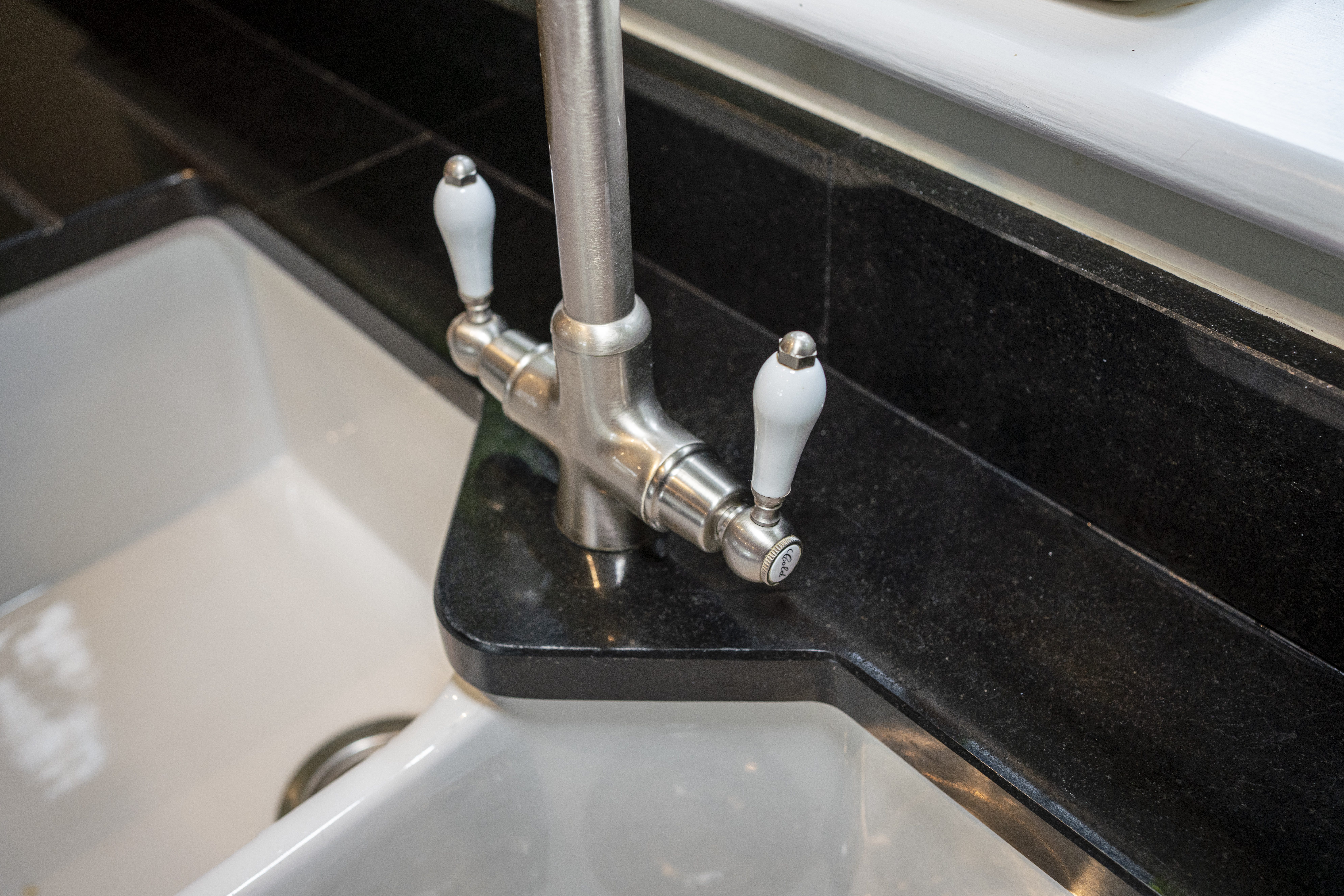 Close up of a kitchen tap over a sink with Absolute Black Granite worktop and matching Granite upstand, showing the polished finish around the corner.