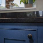 Close up of the polished edge of an Absolute Black Granite worktop above blue cabinetry, showing subtle Granite speckling and a clean straight profile.