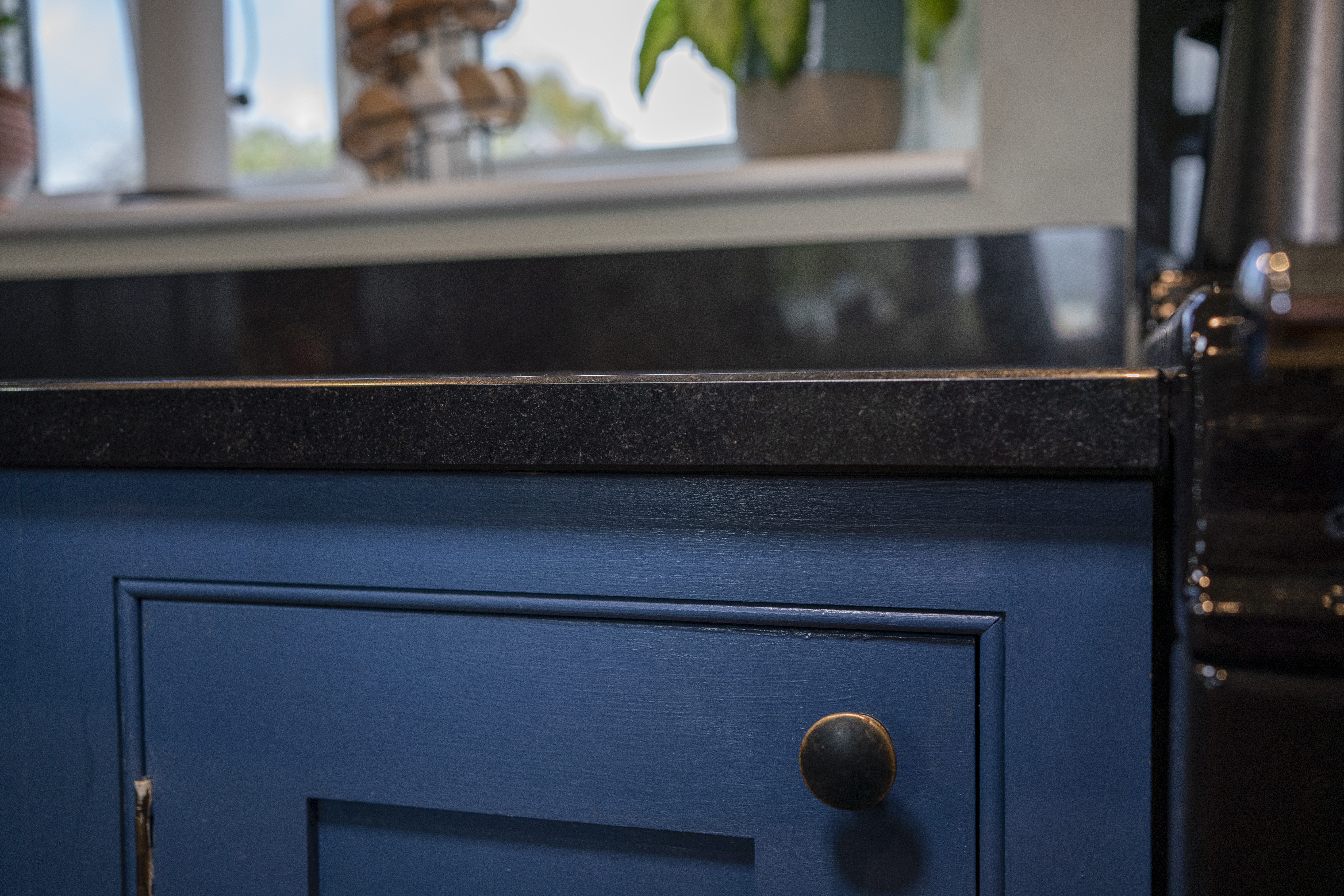 Close up of the polished edge of an Absolute Black Granite worktop above blue cabinetry, showing subtle Granite speckling and a clean straight profile.