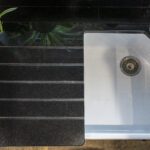 Close up of Absolute Black Granite worktop with precision cut drainer grooves next to a white sink, showing the polished finish and clean lines.