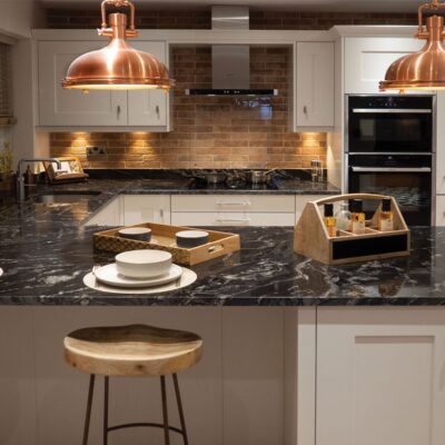 Modern kitchen island with Black Storm Granite worktop, showing dramatic veining under pendant lights with bar stools and place settings.