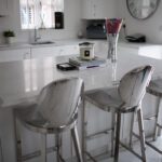 Modern kitchen featuring Statuario Bianco Porcelain island with bar stools and bright white cabinetry
