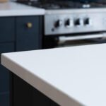 Blanco Zeus Quartz worktop edge close-up showing a crisp white surface above dark blue cabinetry