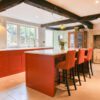 Open-plan kitchen with Supreme Calacatta Quartz island and breakfast bar seating on red cabinetry and exposed beams