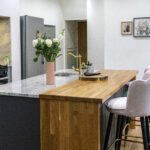 Angled view of an Ivory Fantasy Granite island worktop with sink, showing the Granite surface, timber waterfall end and seating area in a modern kitchen.