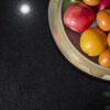 Close up of Absolute Black Granite worktop surface with a bowl of fruit, showing the consistent black tone and light reflection on the polished finish.