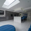 Modern open plan kitchen with White Calacatta Quartz island and blue bar stools under a large skylight