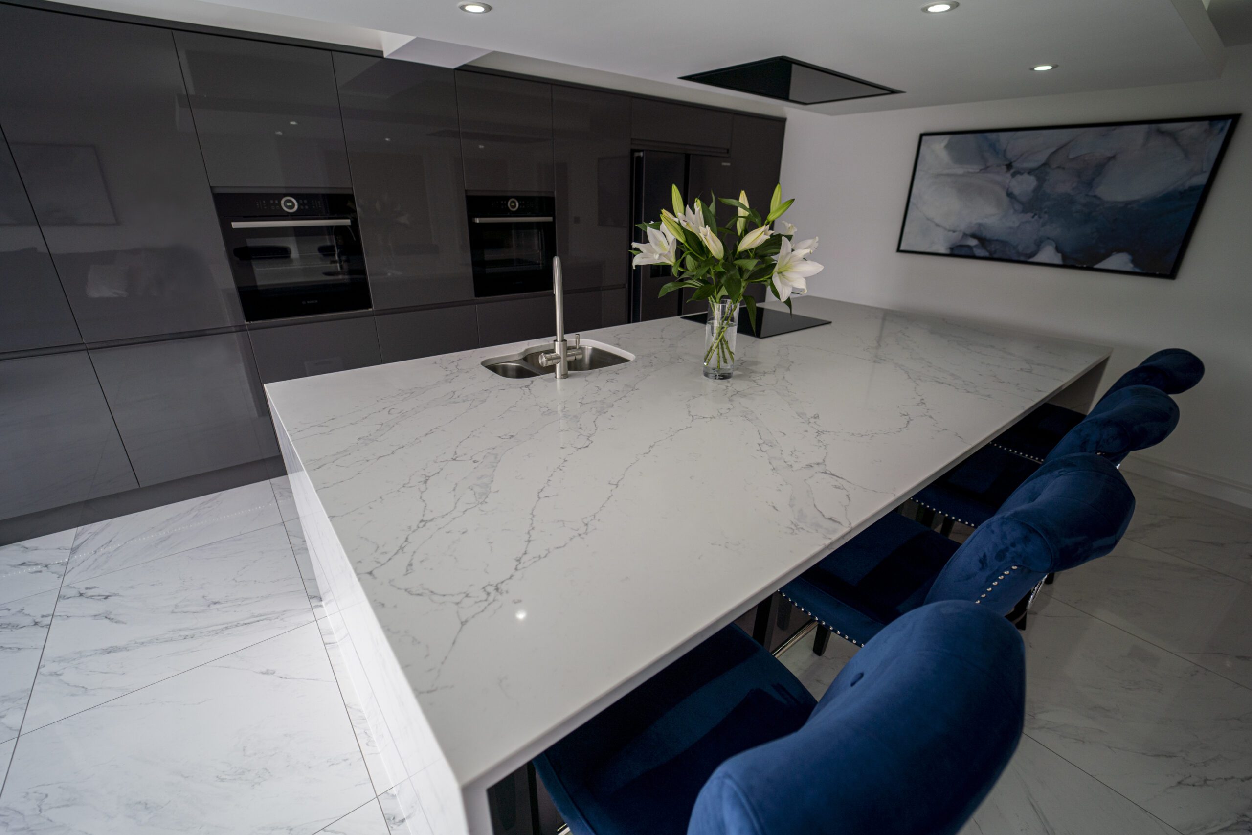 White Calacatta Quartz kitchen island with blue bar stools and floral arrangement on the worktop