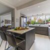Open-plan kitchen with Blanco Zeus Quartz island worktop and bright white surface with seating in front of large windows