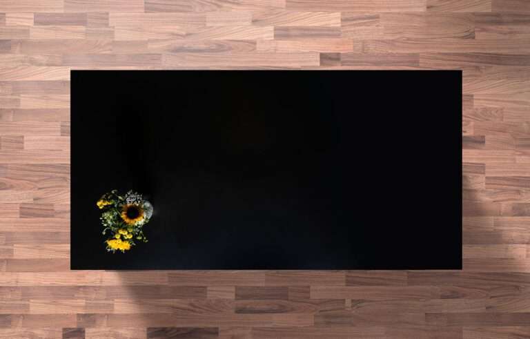 Magma Black Granite worktop sample with a sunflower bouquet on the corner above a wood-effect surface
