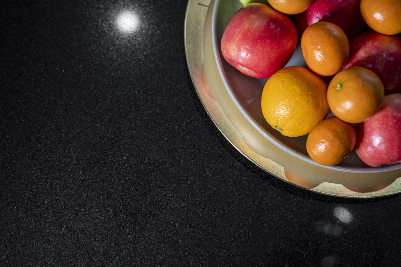 Close up of polished Absolute Black Granite worktop with a fruit bowl in the corner, showing the deep black colour and reflective finish.