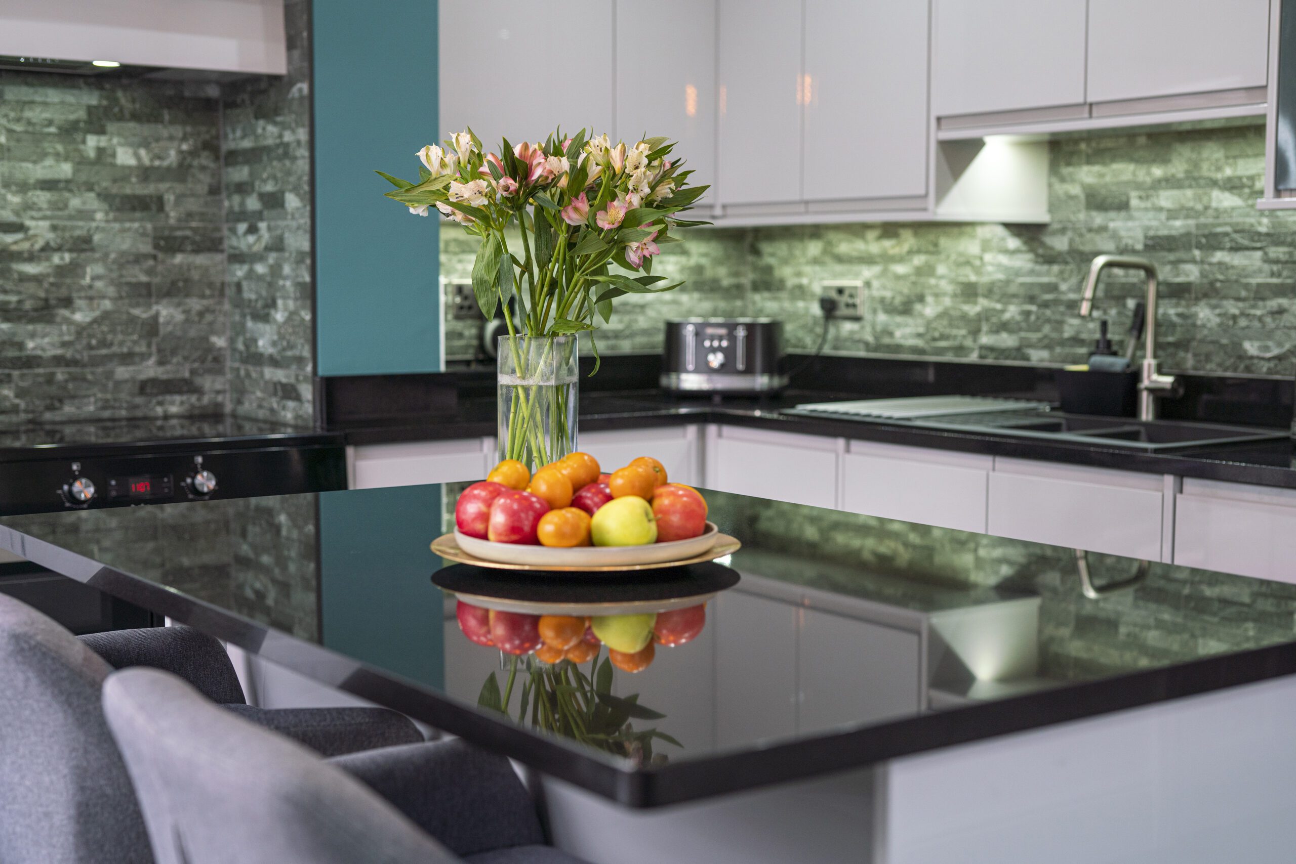 Kitchen island with polished Absolute Black Granite worktop, styled with a fruit bowl and flowers, showing the reflective black surface.